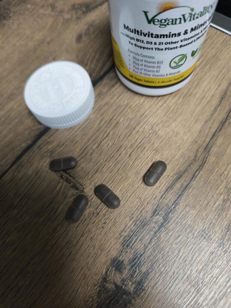 Bouteille de compléments alimentaires ouverte sur une table en bois, avec quatre gélules à côté.