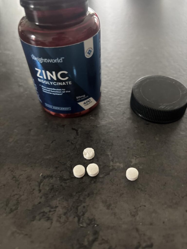 Le produit est une bouteille de zinc bisglycinate de la marque WeightWorld, posée sur une surface sombre avec quelques compri...