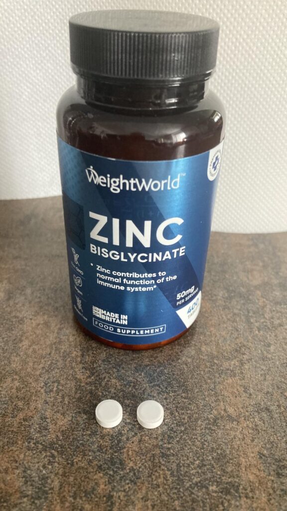 Le produit est une bouteille de zinc bisglycinate de la marque WeightWorld, posée sur une surface claire avec deux comprimés...