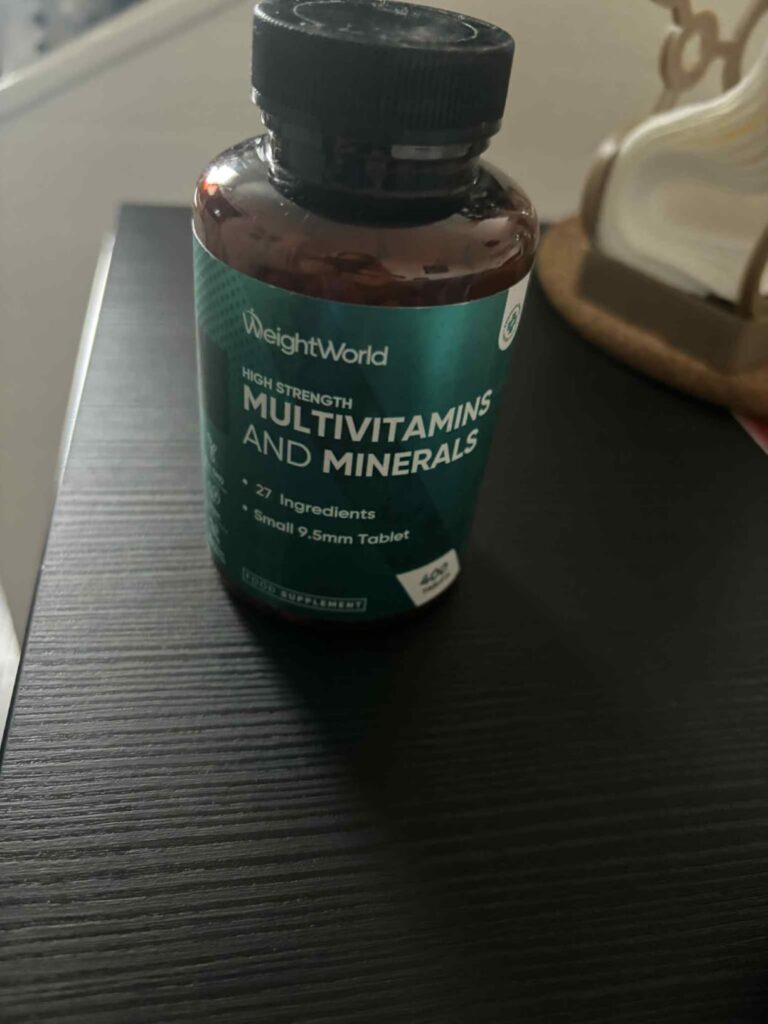 Le flacon de multivitamines est posé sur une table de chevet en bois foncé.