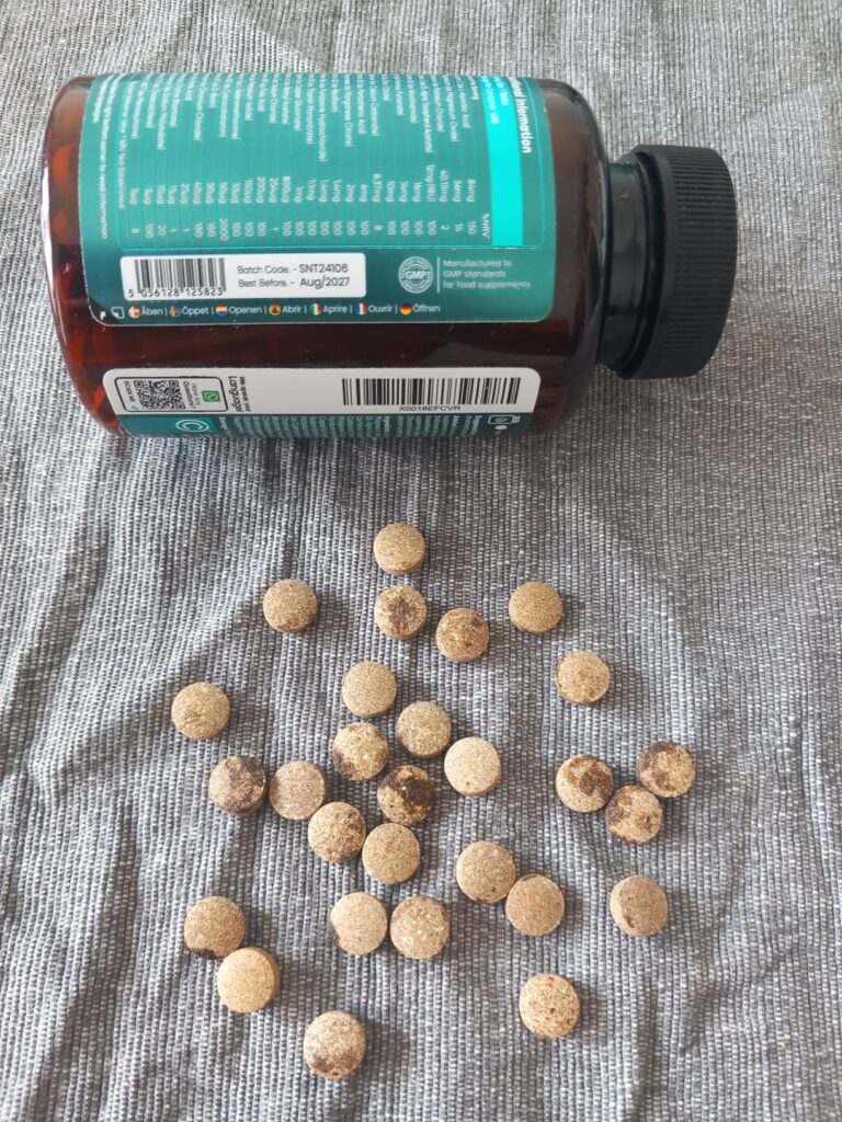 Le flacon de multivitamines est posé sur le côté, avec des comprimés répandus devant lui sur un tissu gris.