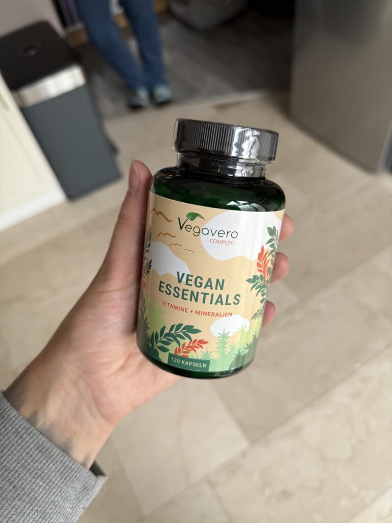 Main tenant la bouteille de pilules Vegan Essentials, vue légèrement de côté