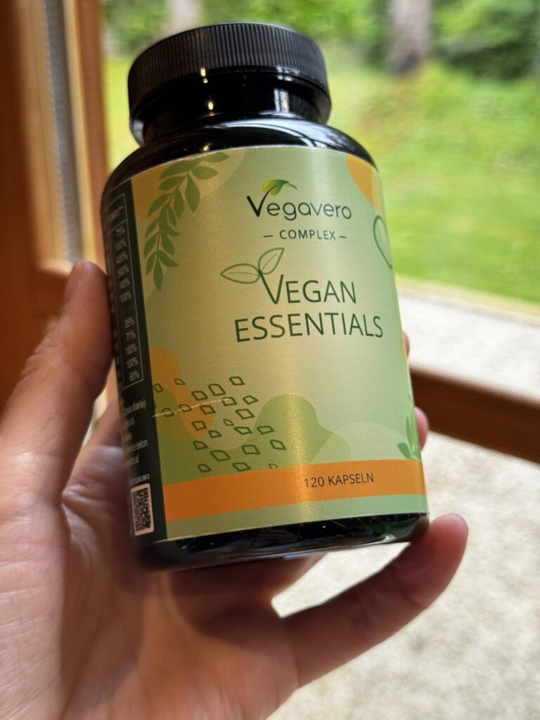 Main tenant la bouteille de pilules Vegan Essentials, vue de face