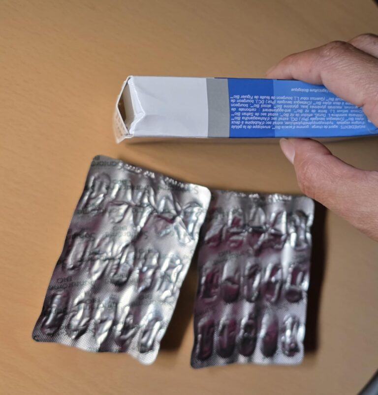 Boîte ouverte et deux plaquettes d'ampoules vides, vues de haut. La main tient la boîte.