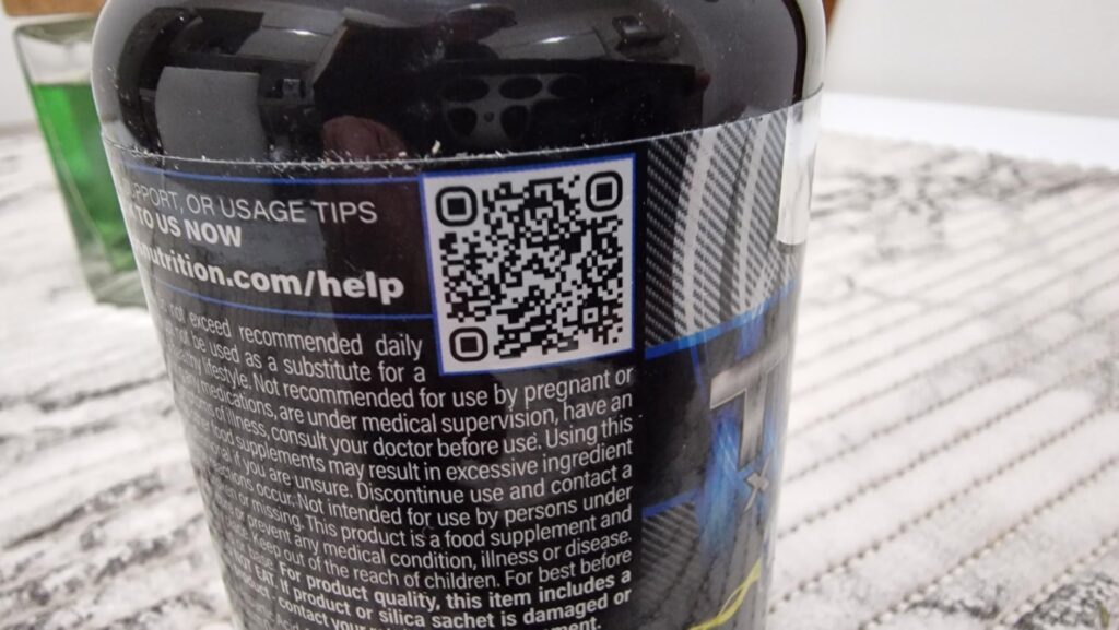 Gros plan sur un QR code et des informations légales imprimés sur l'étiquette d'un flacon de compléments alimentaires.