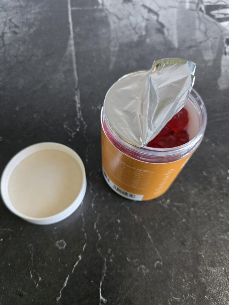 Le pot de vitamines, couvercle ouvert, avec la protection des bonbons arrachée.