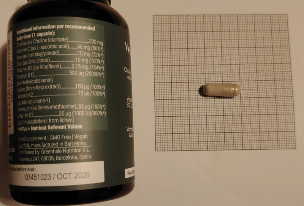 Une gélule posée sur du papier millimétré, à côté d'une bouteille de compléments alimentaires.