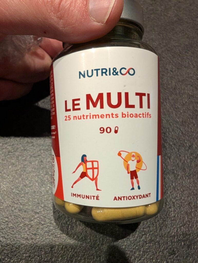 Flacon de compléments alimentaires, étiquette en français, tenu à la main.