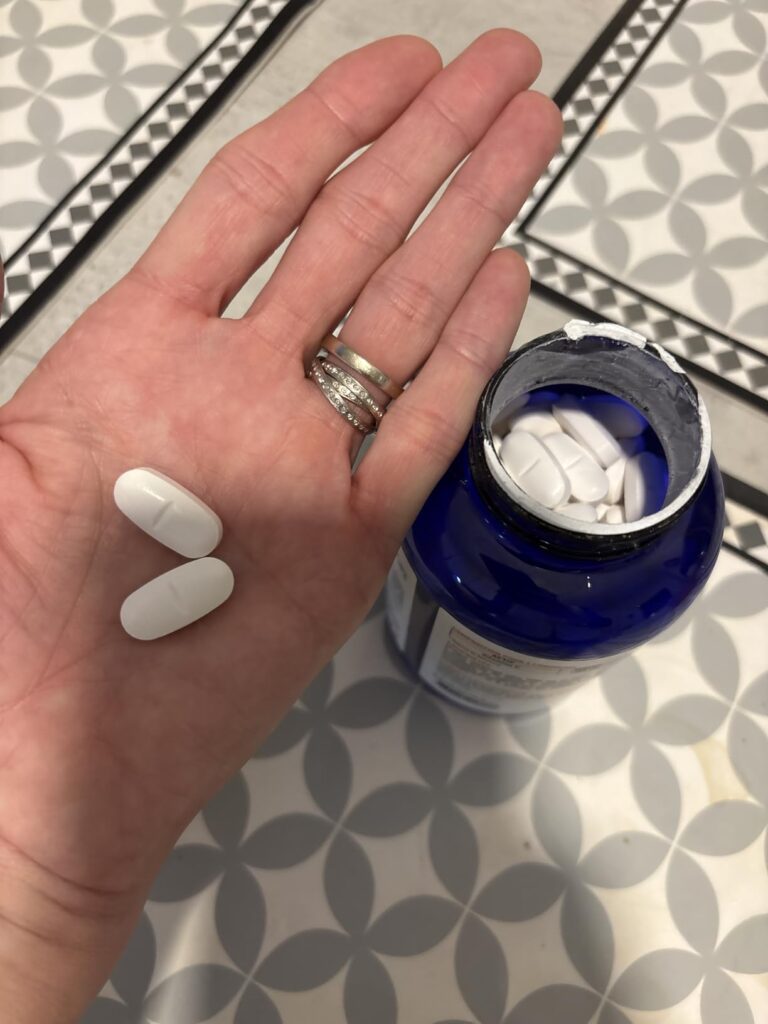 Main tenant deux comprimés de vitamine C, avec la bouteille ouverte en arrière-plan.