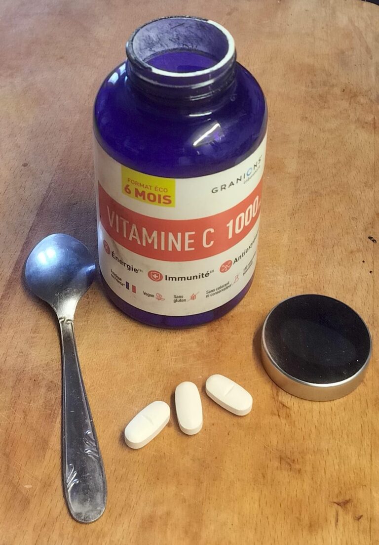 Bouteille de vitamine C sur une table en bois avec trois comprimés et une cuillère.