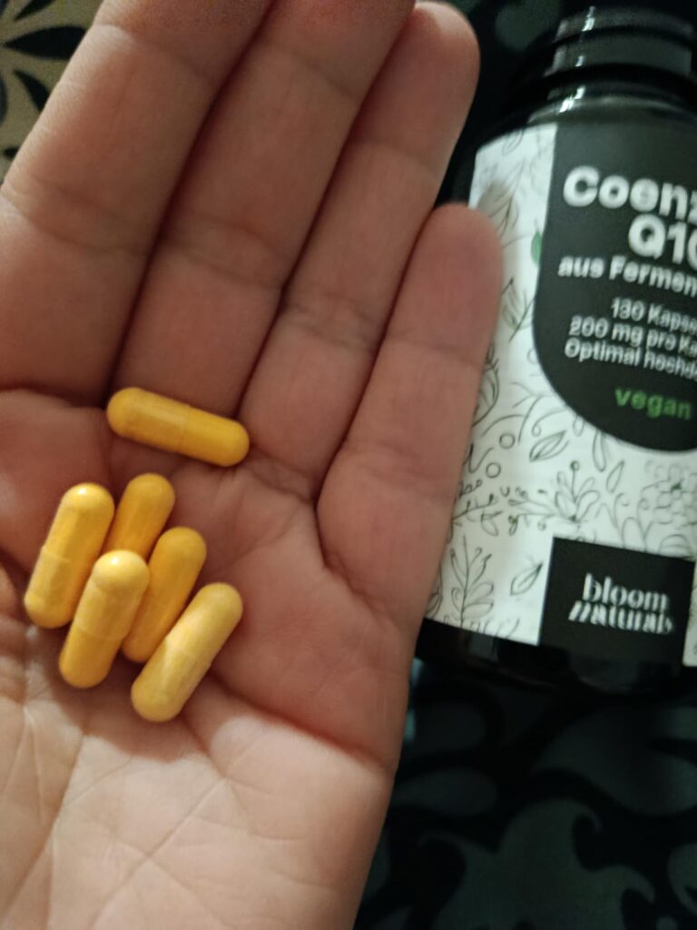 Gros plan sur une main tenant des gélules orange, avec la bouteille floue en arrière-plan. La bouteille est la même que dans...