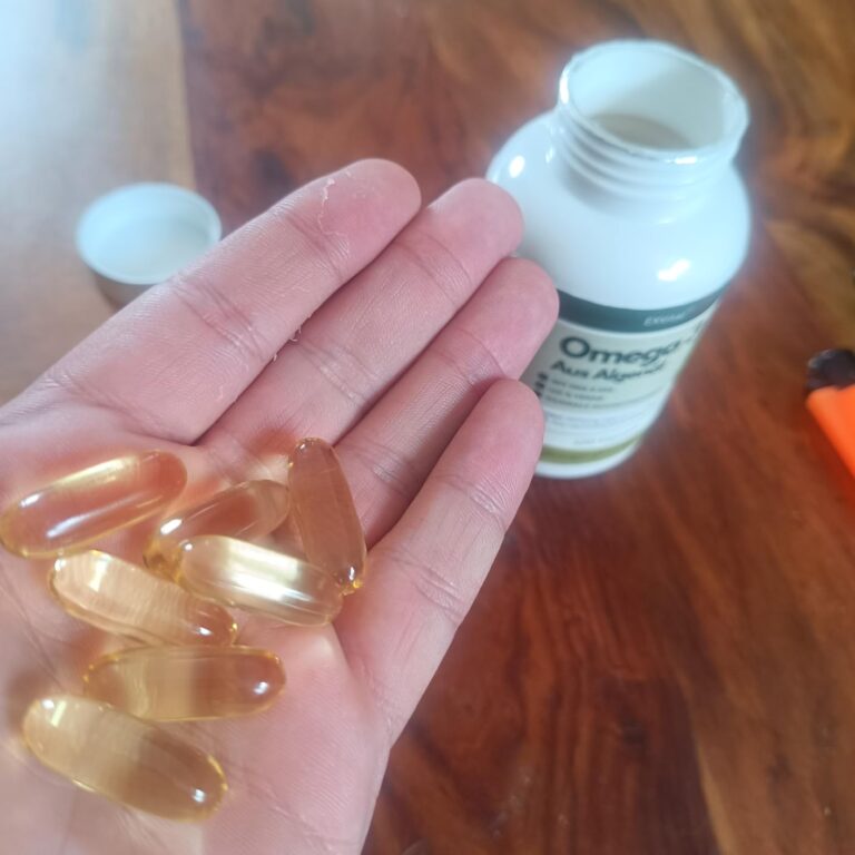 Une main tient des gélules d'Omega 3. Le flacon est en arrière-plan, sur une table en bois.