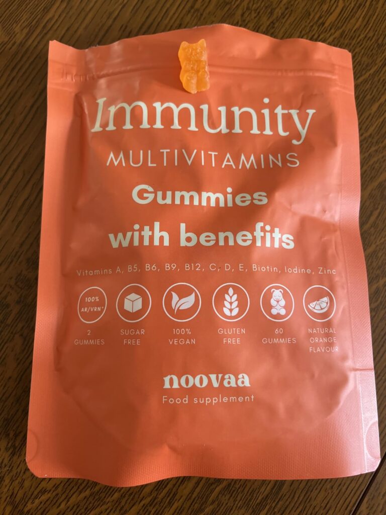 Sachet de compléments alimentaires Noovaa, multivitaminés pour l'immunité, saveur orange. Un gummy est posé sur le sachet.