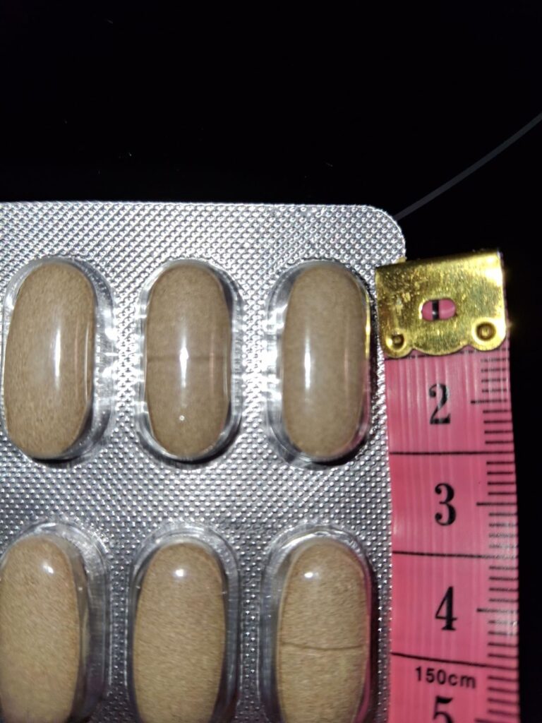 Gros plan sur une plaquette de gélules avec un mètre ruban rose à côté, mesurant la largeur des capsules. Même type de photo...