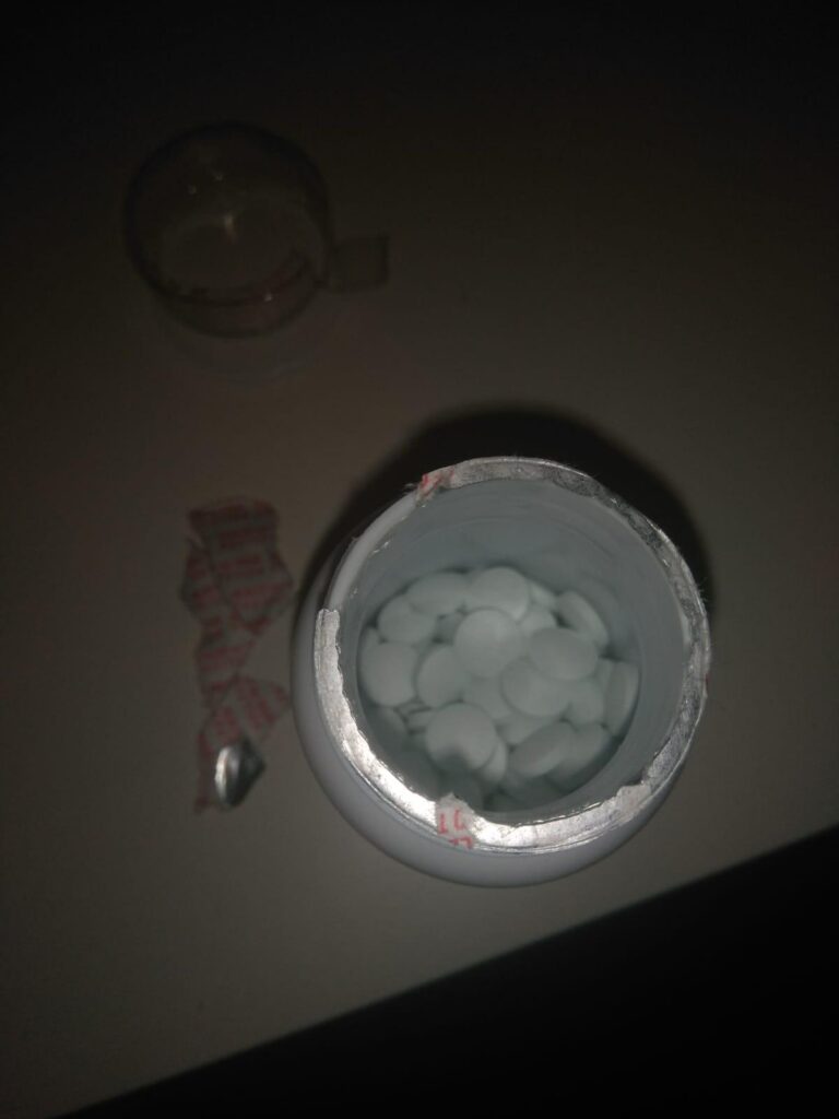 L'intérieur du pot de compléments, avec les pilules blanches et le sceau de protection déchiré.