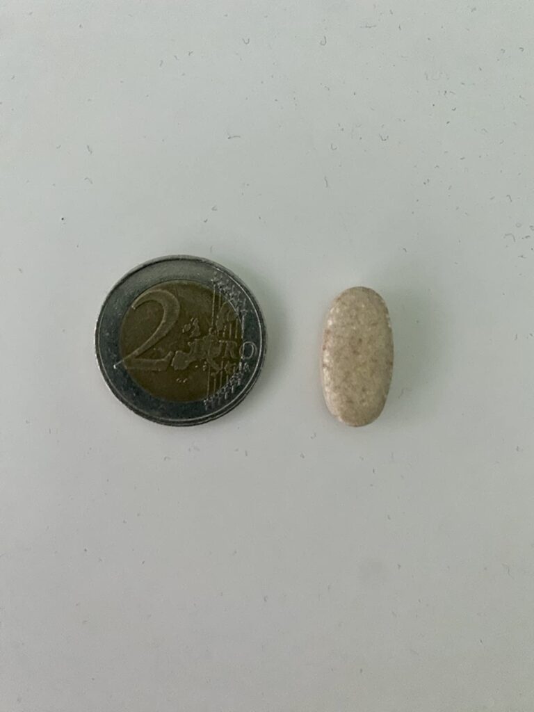 Un comprimé 'One-A-Day' à côté d'une pièce de 2 euros pour comparer la taille.