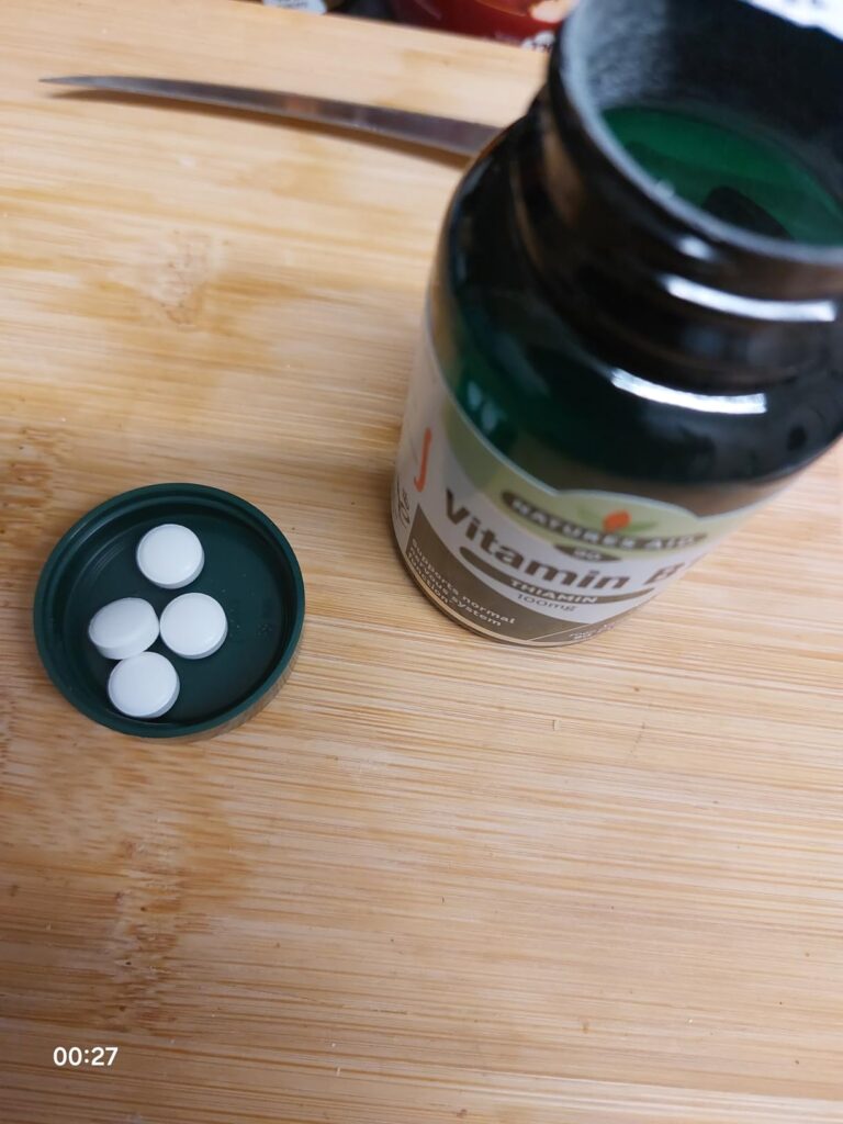 Quatre comprimés de vitamine B1 dans le bouchon du flacon, posés sur une planche de bois. Le flacon est ouvert.