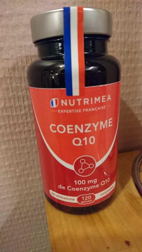Flacon de compléments alimentaires sur une table en bois, étiquette visible. Un ruban tricolore (bleu, blanc, rouge) est coll...