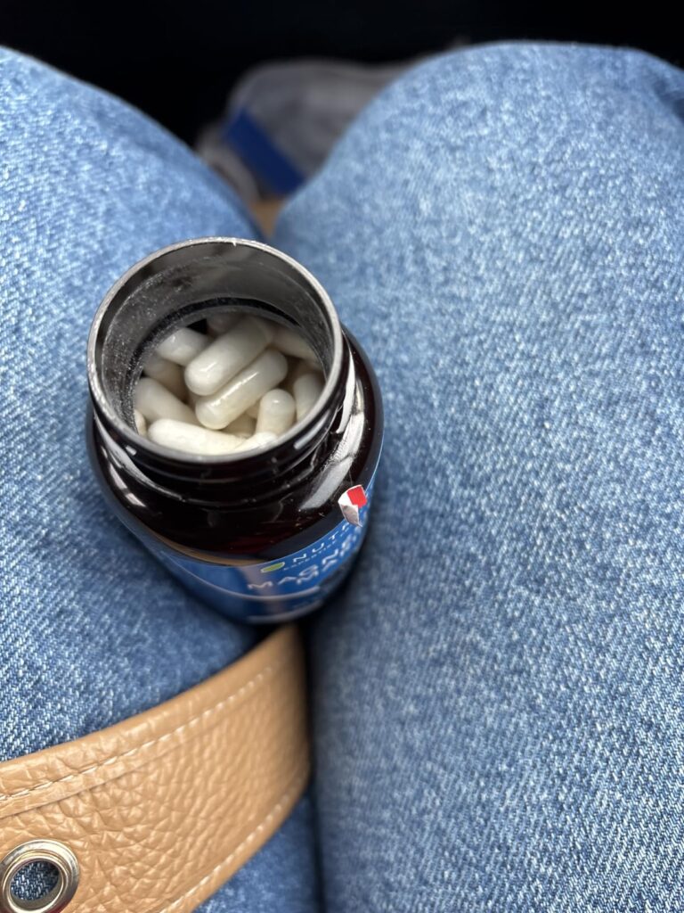 Bouteille de compléments alimentaires ouverte posée sur les genoux d'une personne dans une voiture, montrant les gélules à l'...