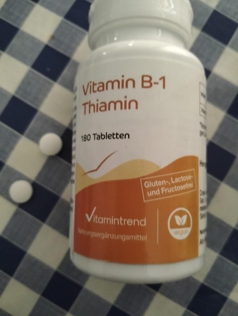 Bouteille de vitamines B1 sur fond de nappe à carreaux, avec deux comprimés à côté.