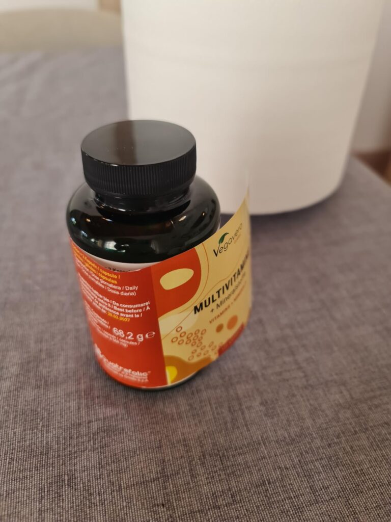 Bouteille de compléments alimentaires posée sur une table, montrant une partie de l'étiquette dépliée. La vue est rapprochée...
