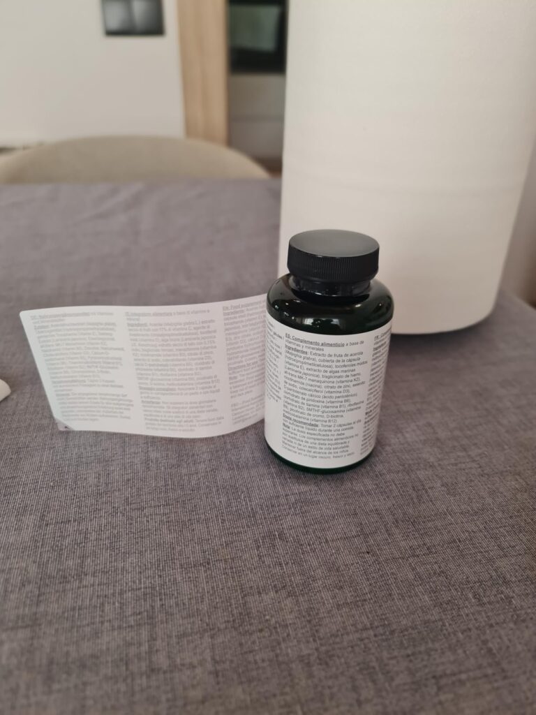 Bouteille de compléments alimentaires posée sur une table, avec l'étiquette dépliée à côté, montrant le texte détaillé des in...