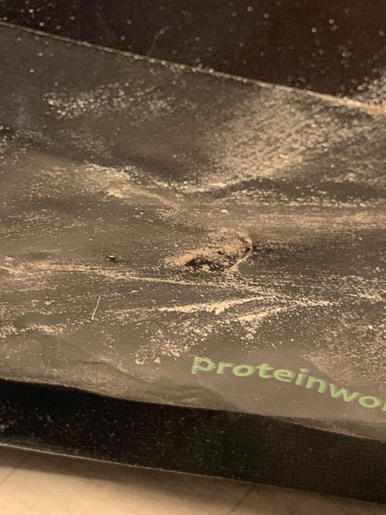 Gros plan sur le haut du sachet de protéine, on peut voir que le sachet est déchiré au milieu, la poudre est visible sur tout...
