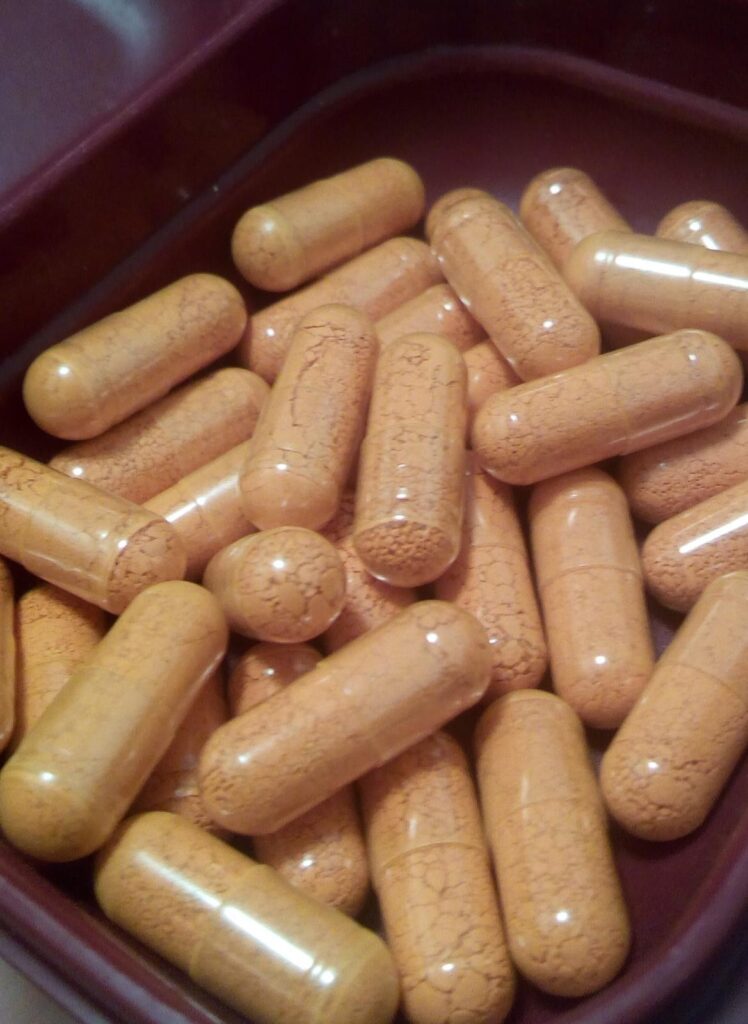 Gros plan sur les gélules de curcuma ouvertes ou transparentes, montrant la poudre orangée à l'intérieur.