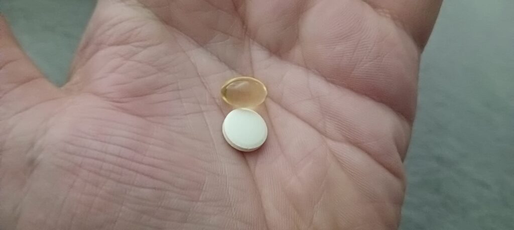 Une pilule blanche et une gélule jaune dans la paume d'une main.