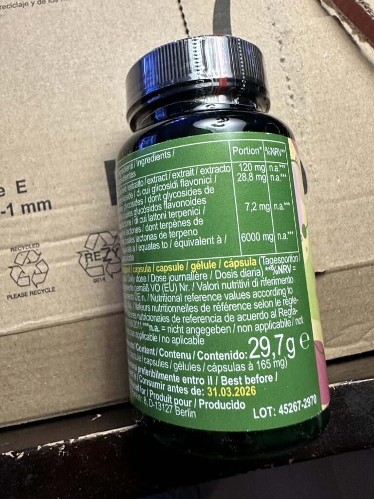 L'arrière d'une bouteille verte de compléments alimentaires posée sur un carton d'emballage Amazon. On y voit la composition...