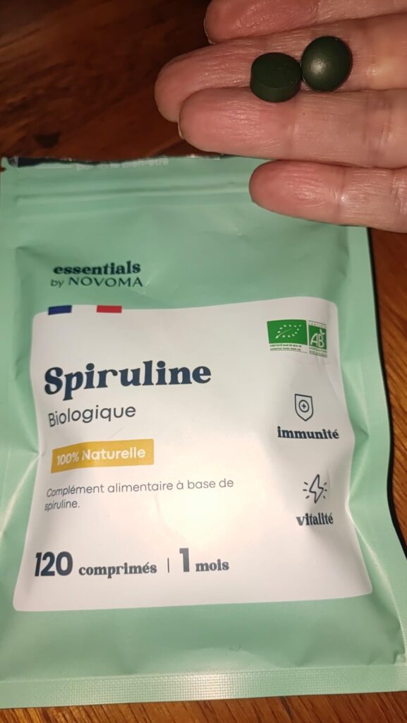 Deux comprimés de spiruline sont montrés dans une main au-dessus du sachet.