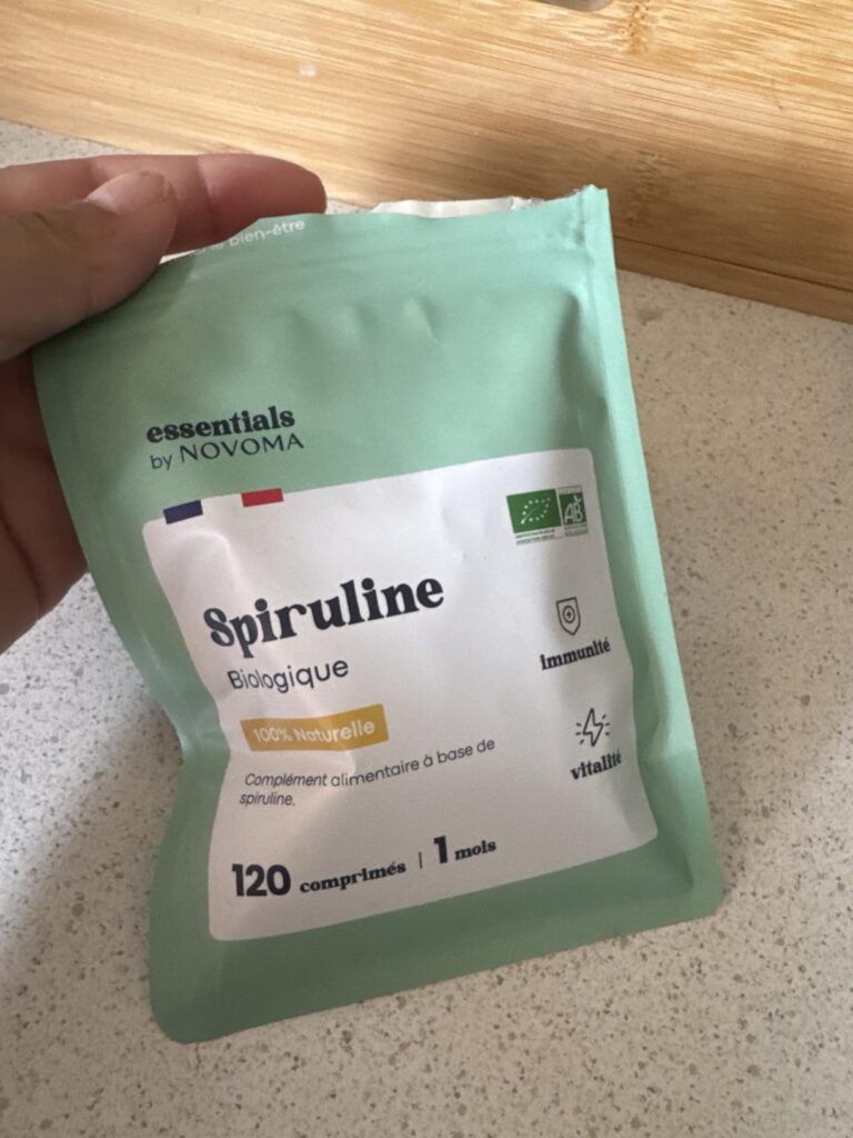Une main tient le sachet de spiruline au-dessus d'un plan de travail clair.