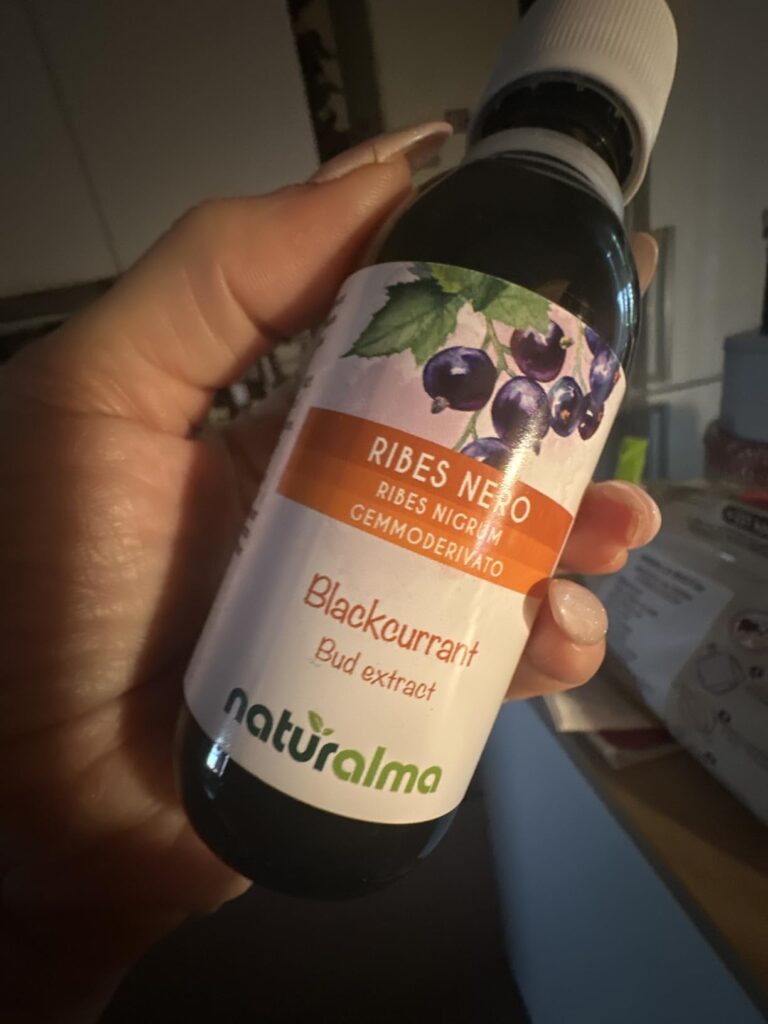 Bouteille d'extrait de bourgeons de cassis tenue dans une main, fond flou. Visuel très proche du visuel 0.
