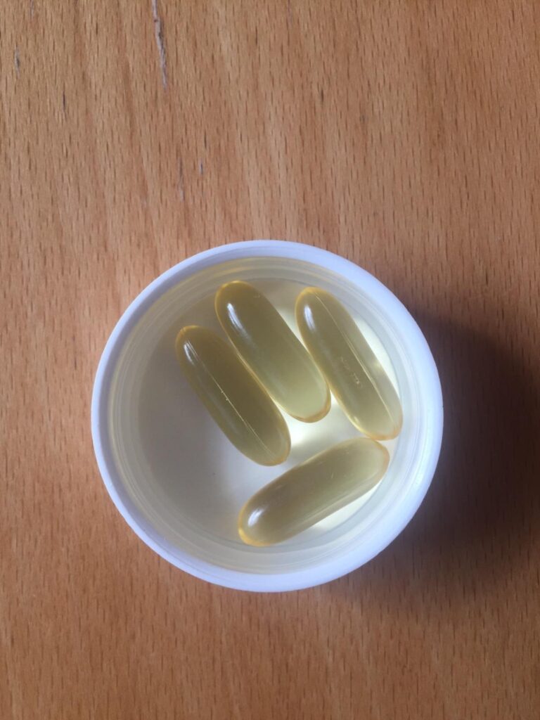 Quatre capsules de compléments alimentaires Omega 3 Algae Oil dans le bouchon blanc du flacon, posées sur une surface en bois...