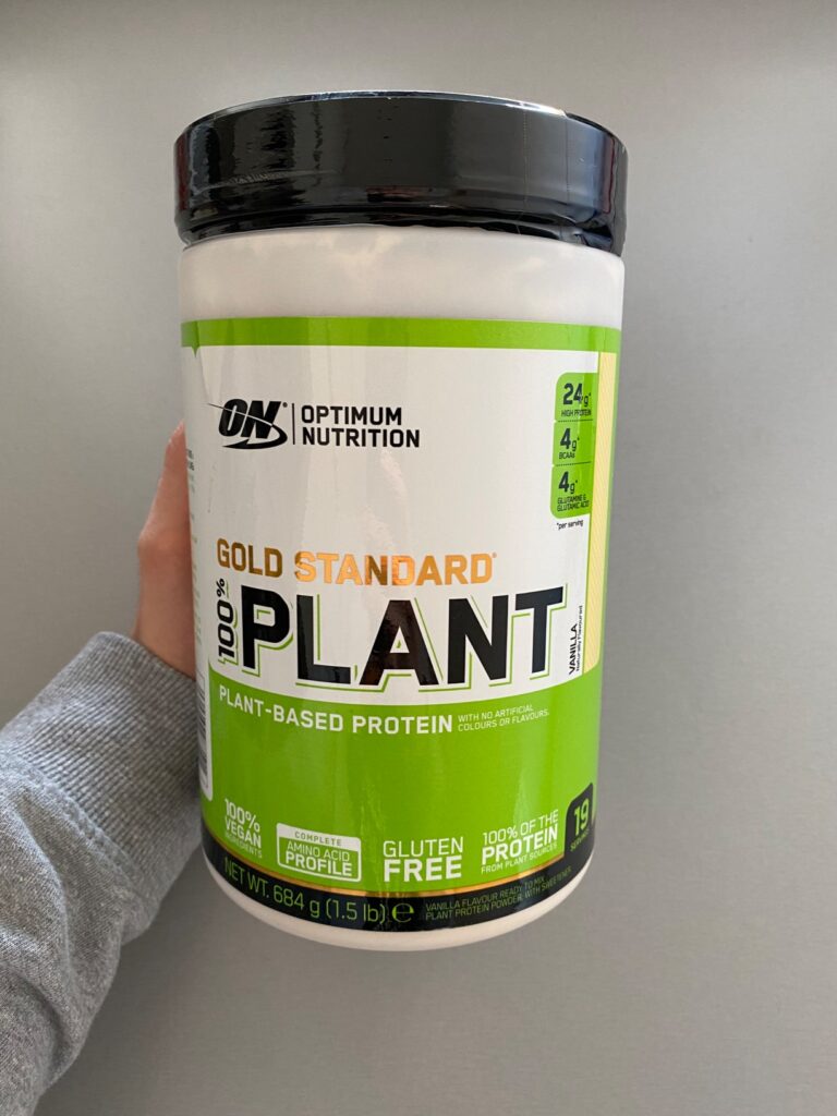 Photo du pot de protéine végétalienne "Gold Standard Plant" tenu à la main.