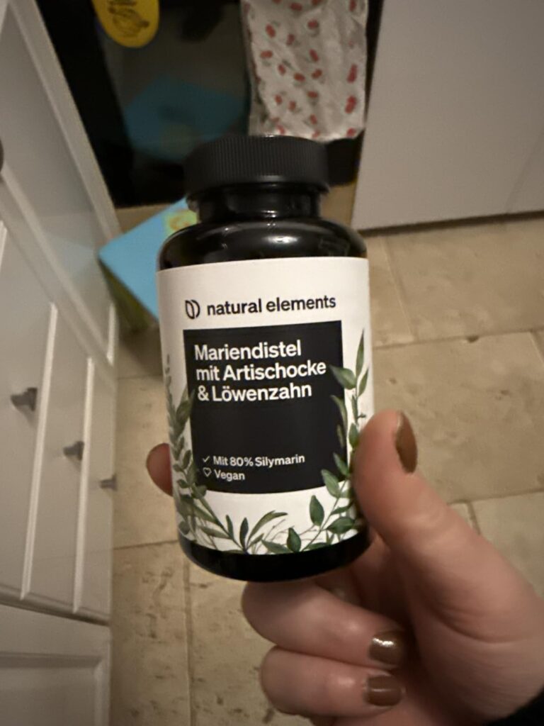 Flacon du produit dans la main, étiquette visible. Dans un intérieur de cuisine.