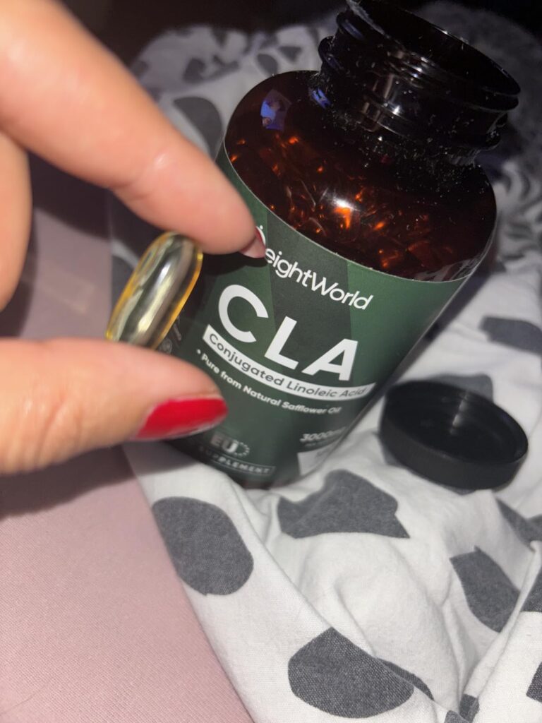Main tenant une gélule de CLA près de la bouteille sur un tissu.