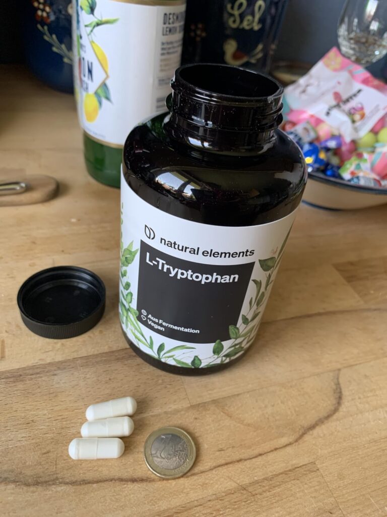 Bouteille de L-Tryptophan ouverte, trois gélules de L-Tryptophan, et une pièce de 1 euro à côté. Le tout est posé sur un plan...