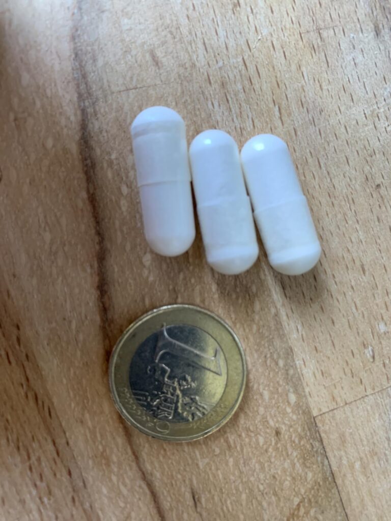 Trois gélules de L-Tryptophan et une pièce de 1 euro à côté, sur un plan de travail en bois. Gros plan sur les objets.
