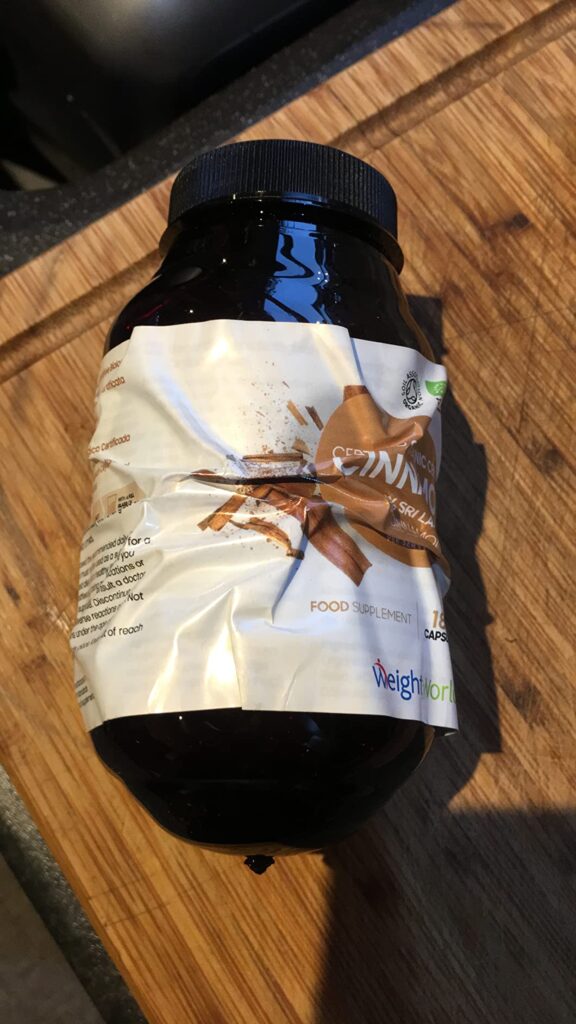 Flacon de compléments alimentaires WeightWorld "Certified Organic Cinnamon" avec l'étiquette abîmée, posé sur une planche en...