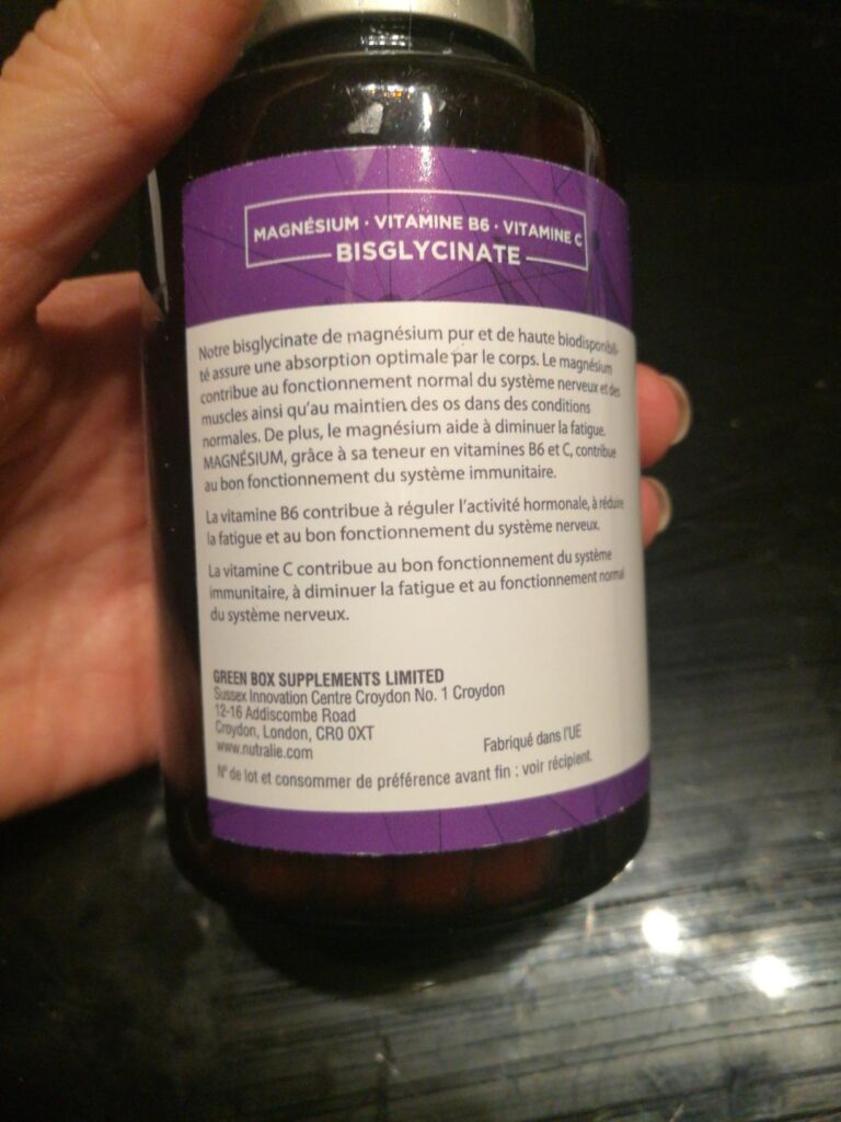 Le côté du flacon, avec les allégations santé et les coordonnées du fabricant, tenu à la main.