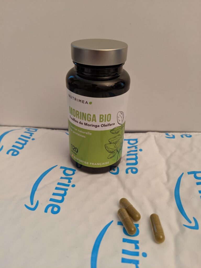Le flacon de gélules de Moringa BIO Nutriméa, posé sur un emballage Amazon Prime, avec trois gélules sorties du flacon.