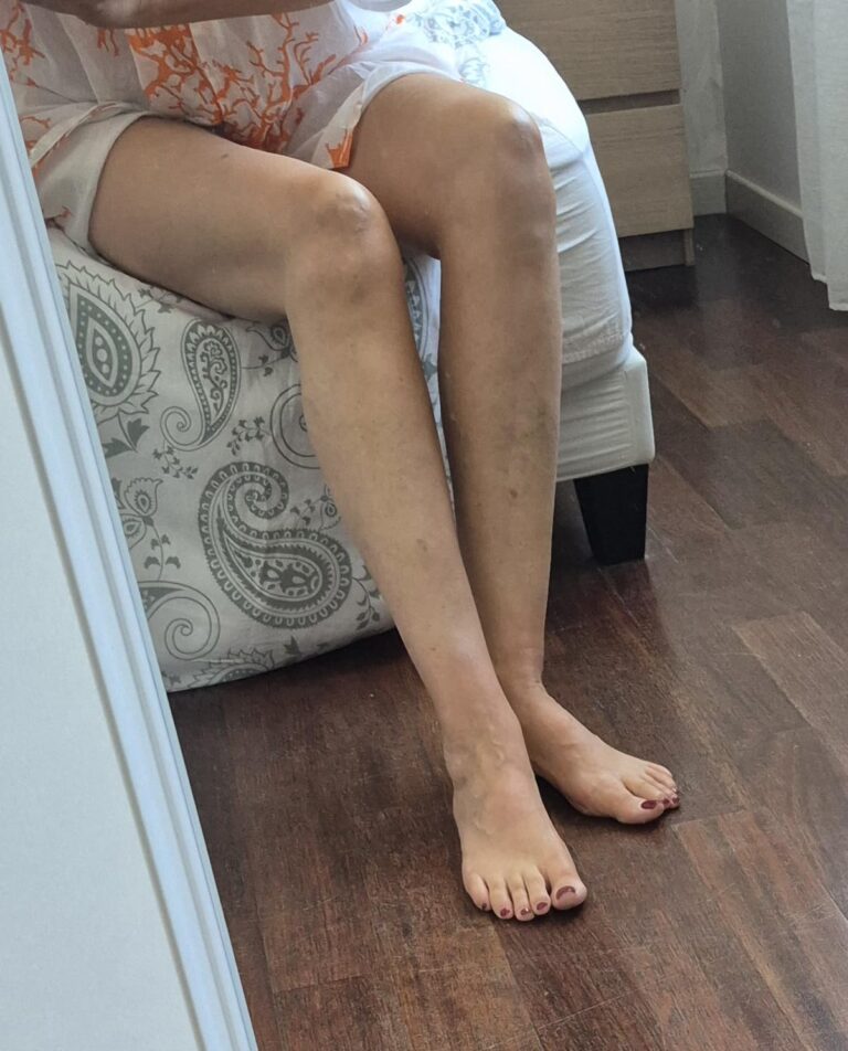 Jambes d'une femme assise sur un fauteuil, pieds nus sur un parquet.