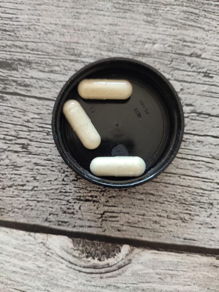 Trois capsules de compléments alimentaires 'Vegan Collagen Advanced' sont posées dans le couvercle noir d'un flacon, sur une...