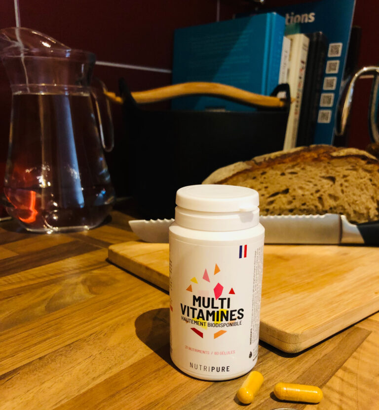Bouteille de multivitamines sur une planche en bois dans une cuisine avec du pain et une carafe.