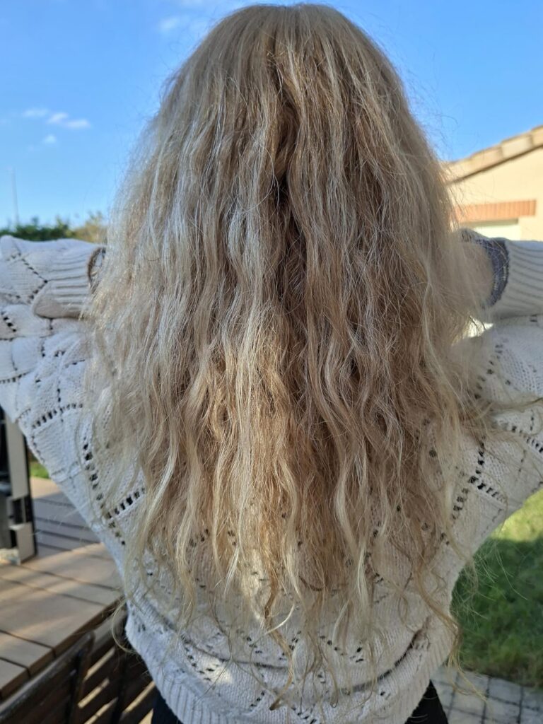 Vue de dos d'une personne aux longs cheveux blonds et ondulés, montrant le résultat après utilisation du produit.