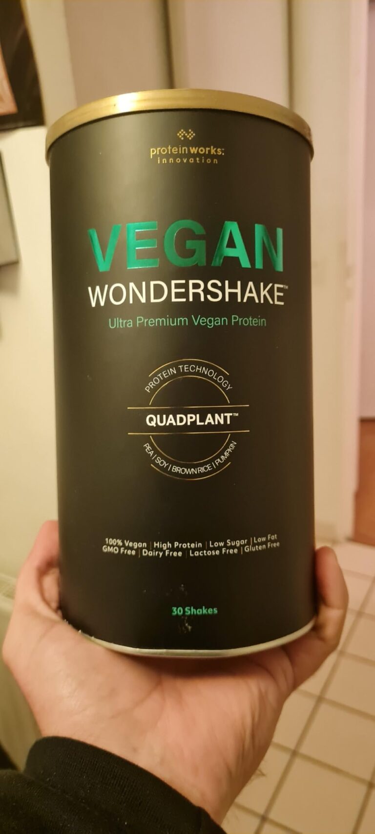 Un pot de "Vegan Wondershake" est tenu dans une main, montrant l'emballage frontal du produit.