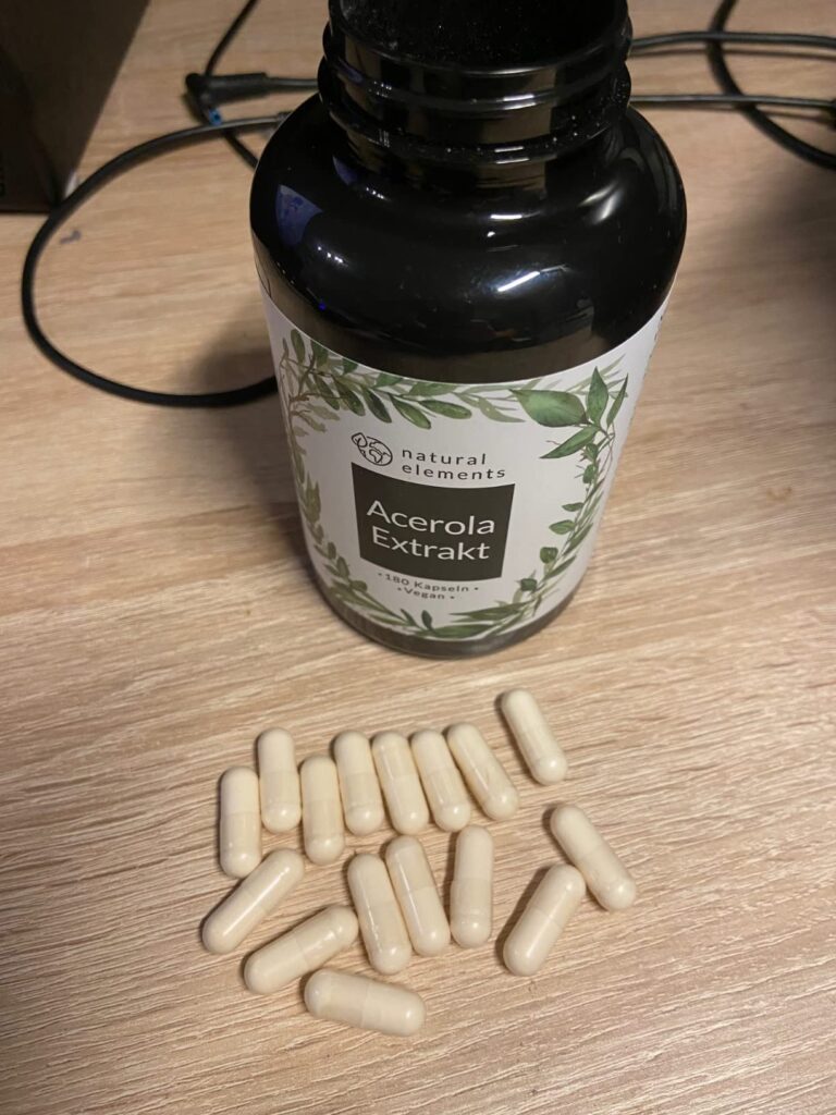 Bouteille de gélules d'acérola et plusieurs gélules éparpillées sur une table en bois.