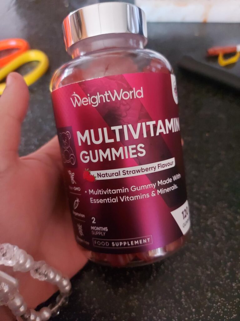 Bouteille de multivitamines WeightWorld tenue à la main, vue de face en léger contre-plongée.