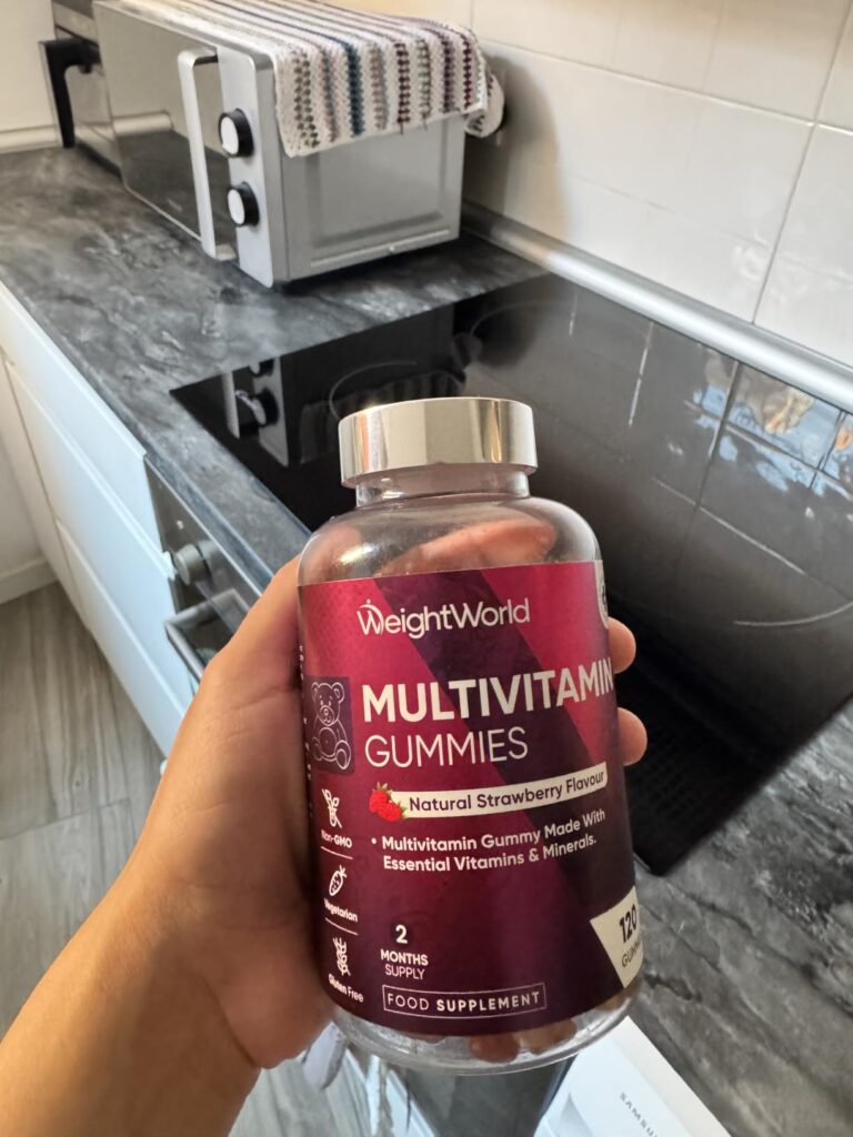 Bouteille de multivitamines WeightWorld tenue à la main, vue de face, en situation dans une cuisine.
